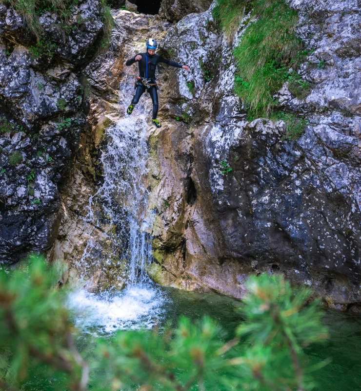 Canyoneer abseiling down a tall waterfall into a clear pool below, surrounded by rocky cliffs and greenery in Fratarica Canyon.
