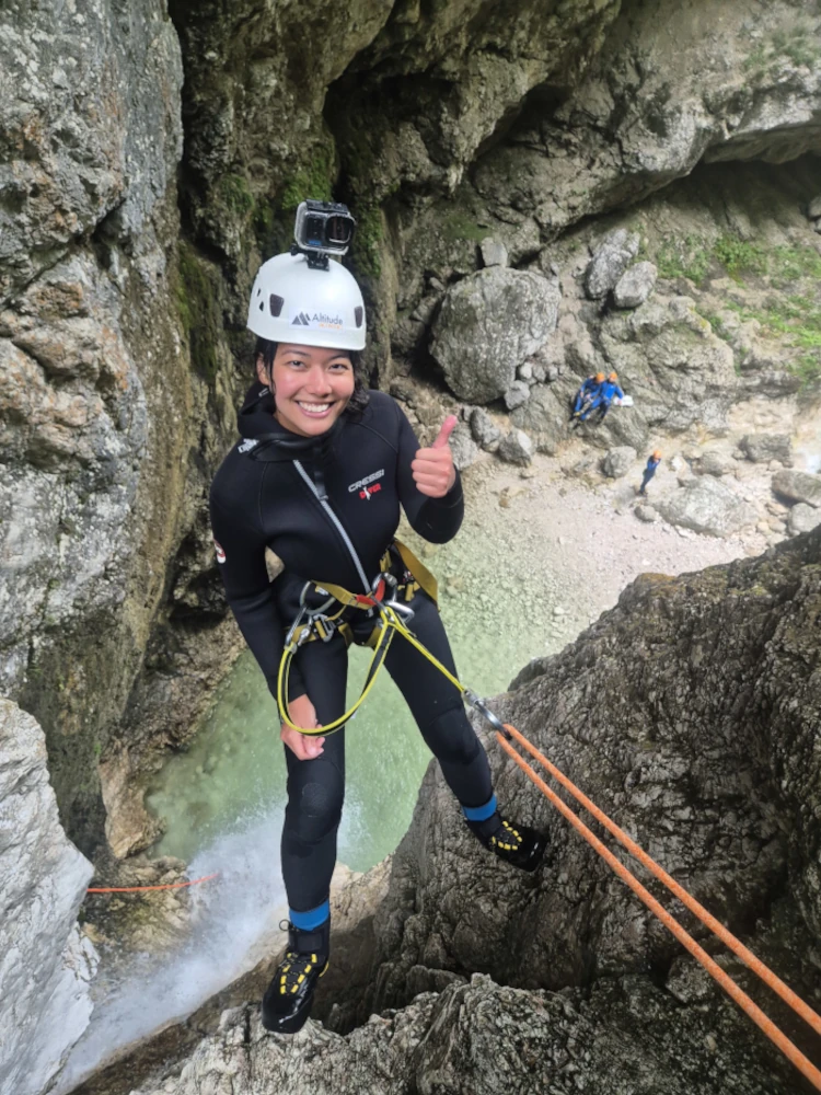 Person in a wetsuit and helmet giving a thumbs-up while rappelling down a rocky canyon wall in Fratarica Canyon.