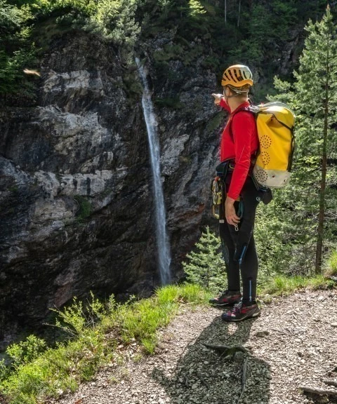 Canyoneer wearing helmet and yellow backpack is pointing at Parabola Waterfall