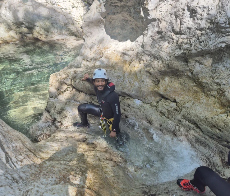 Canyoneer preparing for descent on a rocky ledge in Sušec Canyon, with turquoise water below.