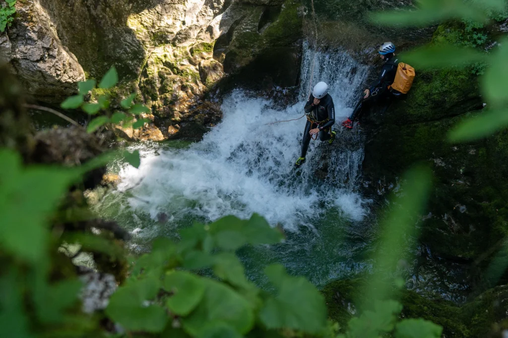 Person sliding down rock into water during Grmecica canyoning Slovenia