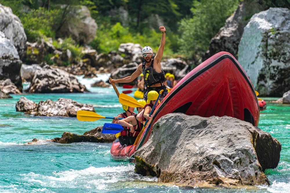 Rafting group navigating turquoise river rapids with guide standing in a red raft among rocky scenery